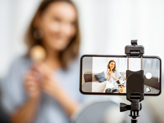 Young woman recording on a smart phone her vlog about cosmetics, showing and demonstrating makeup, close-up on phone. Influencer marketing in social media concept