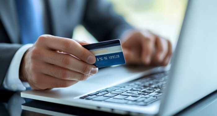 Businessman holding credit card and typing on laptop keyboard, making online payment