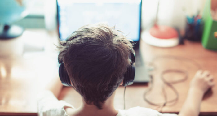 Little dependent gamer kid playing on laptop indoors
