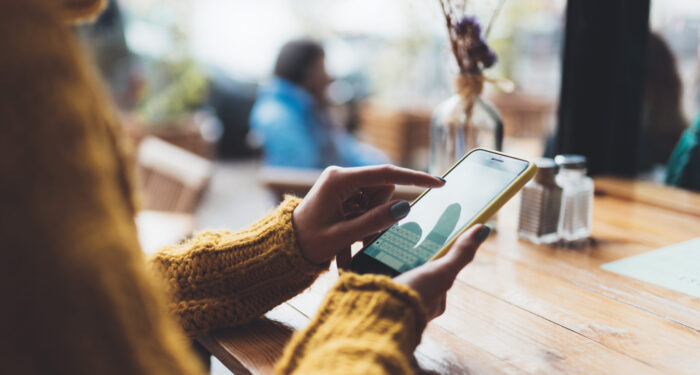 girl hold in hands yellow empty screen mobile phone close up, person type message on smartphone in sun cafe, relax tourist travels planning trip, hipster enjoy journey in cityscape, lifestyle holiday concept, internet online