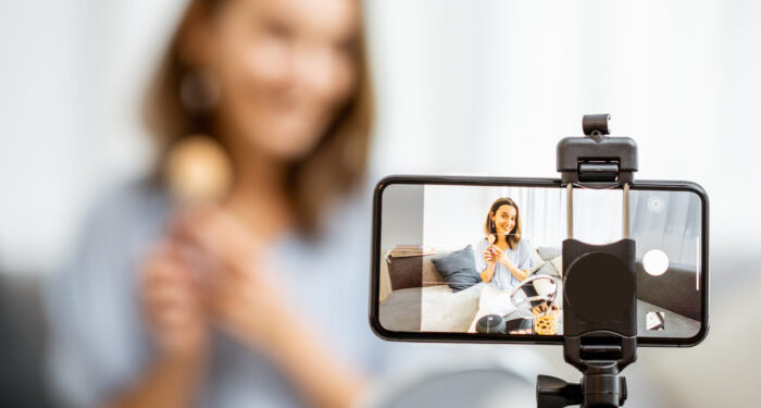 Young woman recording on a smart phone her vlog about cosmetics, showing and demonstrating makeup, close-up on phone. Influencer marketing in social media concept