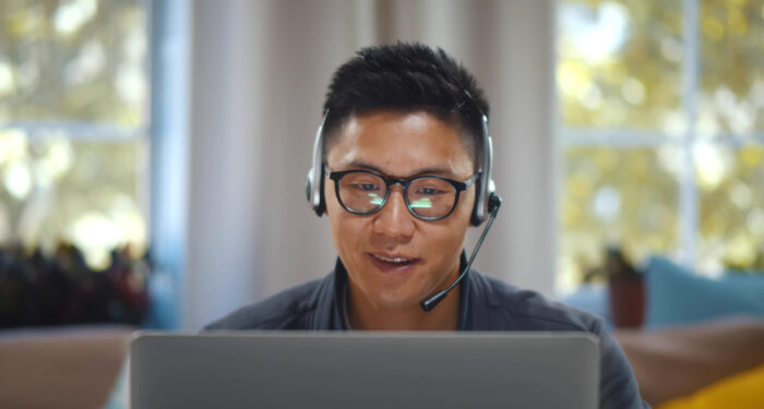Young asian businessman working on laptop in headset having video conference at home. Portrait of handsome freelancer in eyeglasses talking online with clients on computer