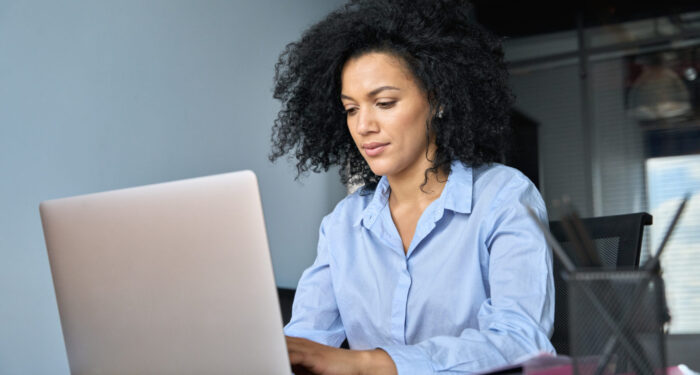 Young serious African American female ceo lawyer businesswoman sitting at desk working typing on laptop computer in contemporary corporation office. Business technologies concept.
