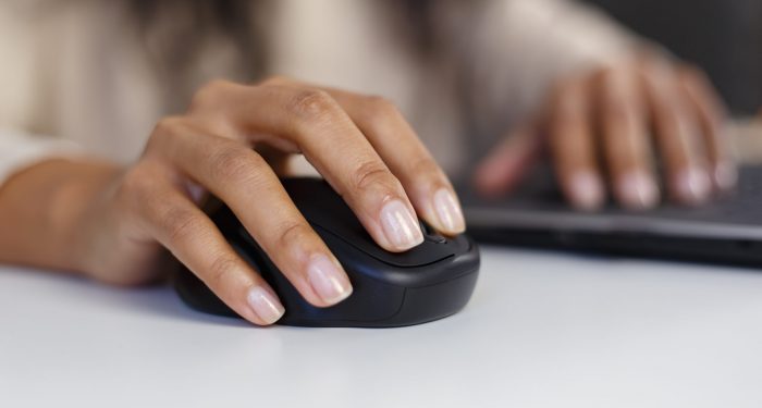 Black woman works on computer. Hands of young adult BIPOC female clicking with modern wireless mouse in close up